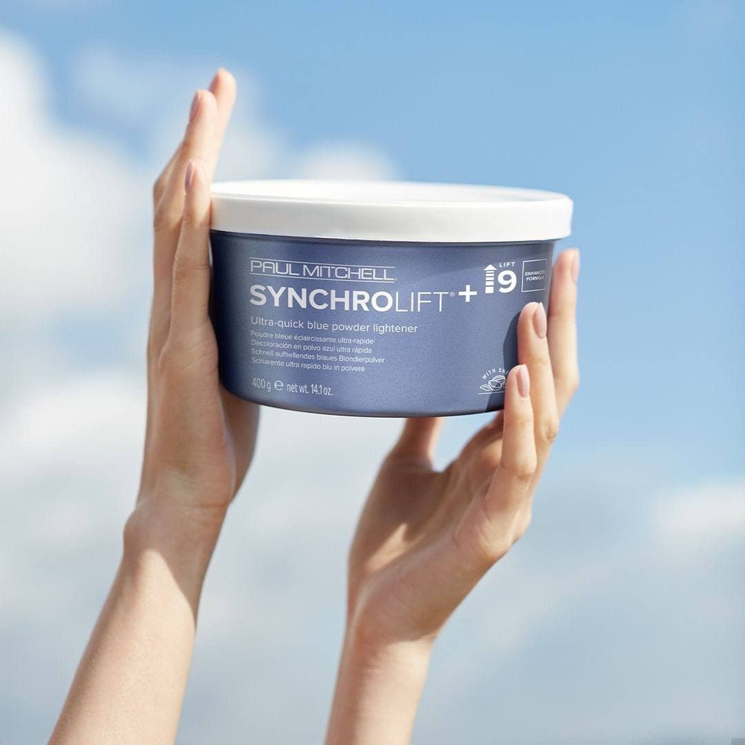 Осветляющая голубая пудра Paul Mitchell SynchroLift+9 в руках на фоне неба